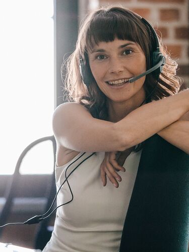 Frau mit Headset lächelt am Arbeitsplatz in Kamera